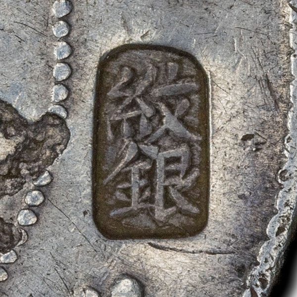 紋銀 - wén yín - fine silver; the Qing benchmark for full-fineness silver, so a statement about the quality of the metal rather than a merchant or shop name - Read top-to-bottom on this vertical stamp as 紋 (wén, 'line, streak, stripe; wrinkle') over 銀 (yín, 'silver'), literally 'patterned silver'. Unlike the shop, partnership and surname marks that make up most compound chops, 紋銀 names a grade of metal rather than a firm. It was the Qing dynasty's benchmark for full-fineness silver, known formally as 戶部庫平十足紋銀 (Board of Revenue treasury-standard full-fineness wenyin) and fixed by the state at a nominal 93.5374 percent silver. In practice it served largely as a unit of account, the notional standard against which real ingots of every other fineness were converted for taxes and commercial reckoning, and it left circulation only when the Nationalist government abolished the tael in favour of the dollar in 1933. The name comes from the surface of the metal: from the late Ming, silver of good quality threw up fine, close-set lines or ripples as a cast ingot cooled, so ingots taken to be of full fineness were called 紋銀 ('pattern silver'), and equivalently 足紋 ('full pattern'). The related Canton trade term 細絲 (sai si, 'fine silk') is where the English word sycee comes from. Struck as a chopmark, the pair therefore reads as an assertion about the coin's silver, roughly 'good, standard-fineness silver', from the merchant, money shop or shroff who tested the piece and passed it. Two cautions are worth keeping. The ripple pattern was never proof of purity, and period accounts record counterfeiters raising artificial threads on substandard ingots by shaking, brushing and blowing the cooling surface. And a chopped foreign coin was not literally 93.5374 percent fine, so the mark is best read as an attestation that the silver was acceptable and of standard quality, not as a measured assay figure.